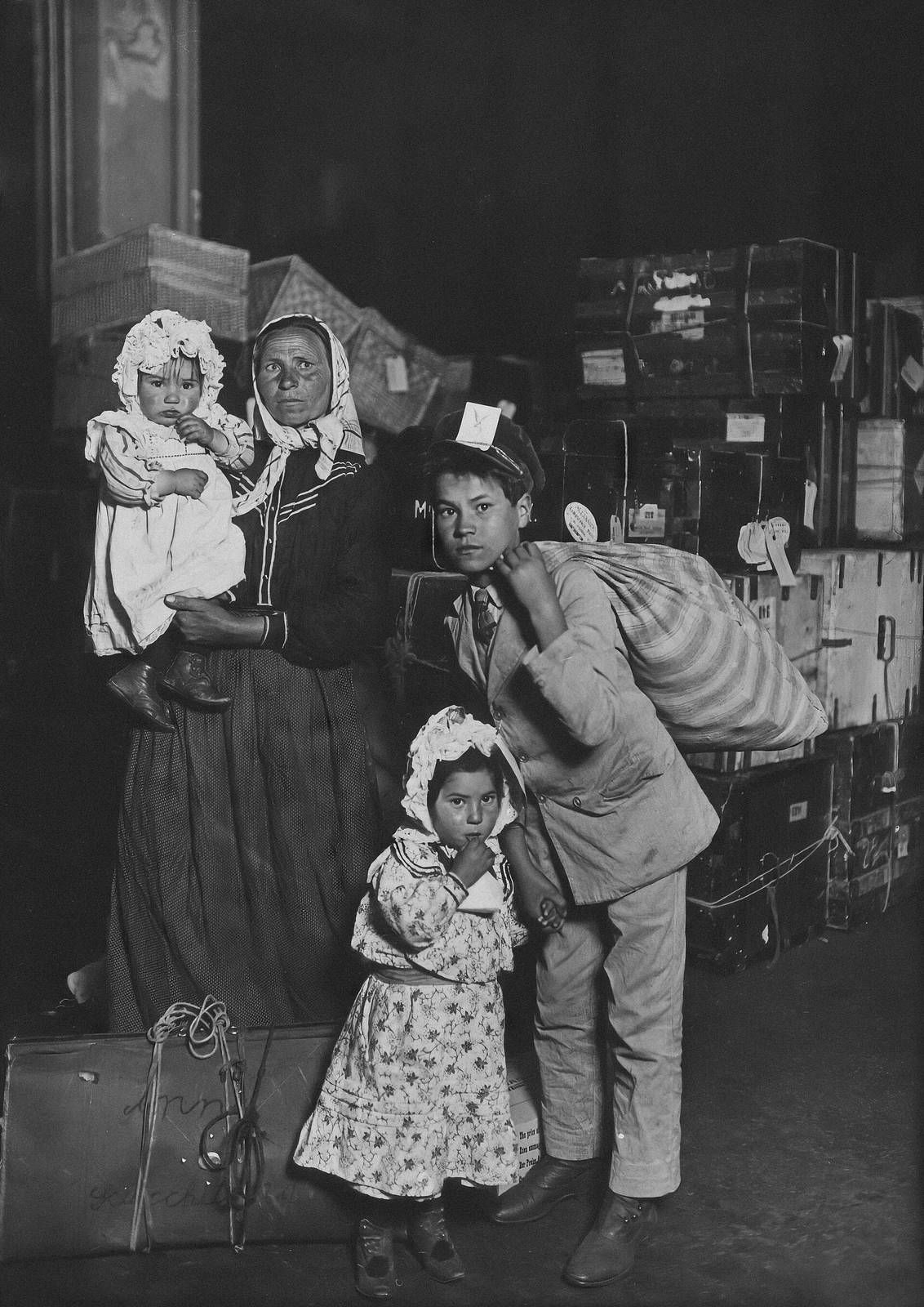 Photograph of an Italian family in the baggage room at Ellis Island in 1905, a woman seated with children.